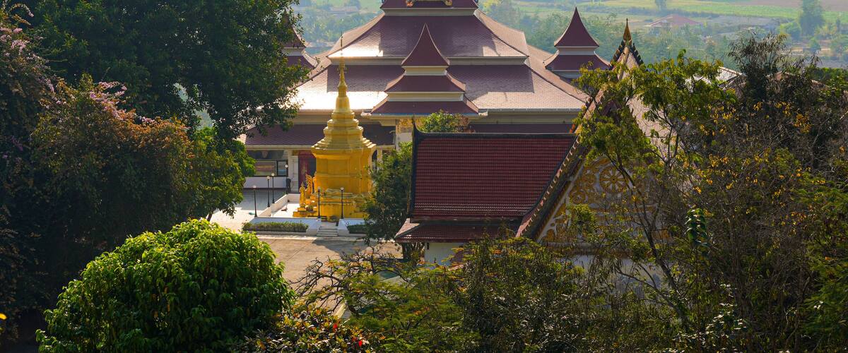 A temple with a golden stupa, surrounded by lush greenery and a view of the countryside.