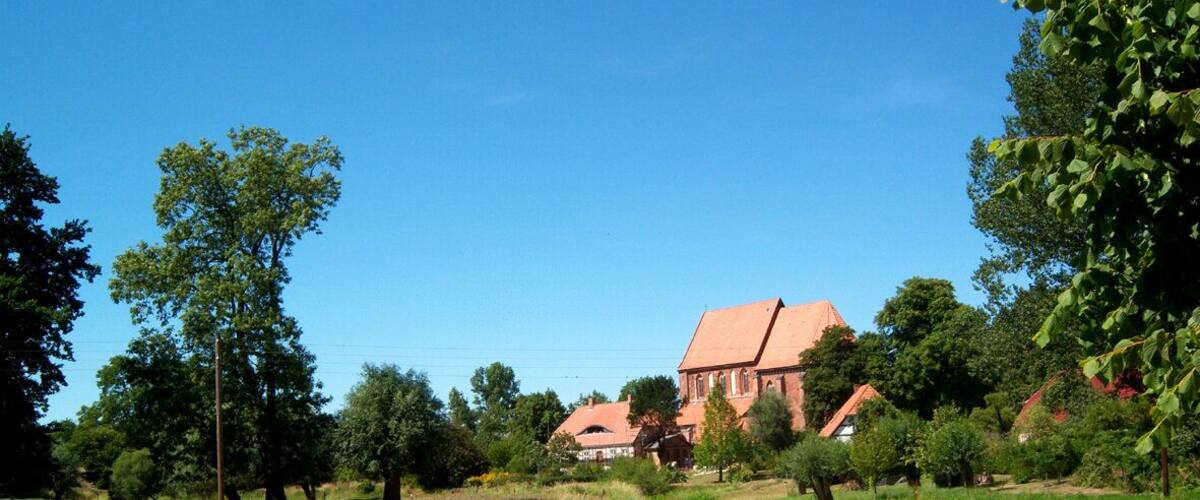 A rural landscape with a large brick building, surrounded by trees and open fields.
