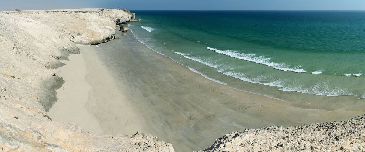A coastal landscape with a sandy beach, rocky cliffs, and calm ocean waves.