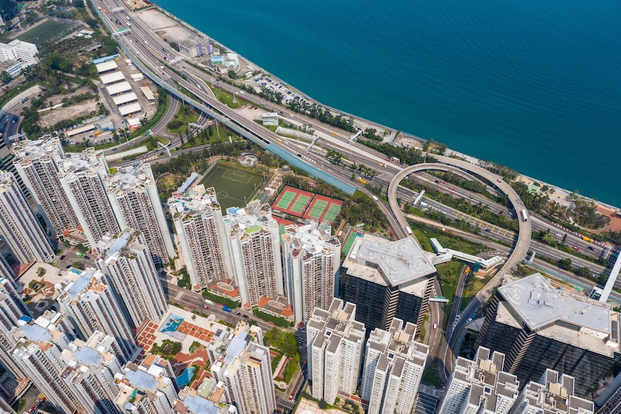 A high-rise urban area with a curved highway, a sports field, and a body of water.