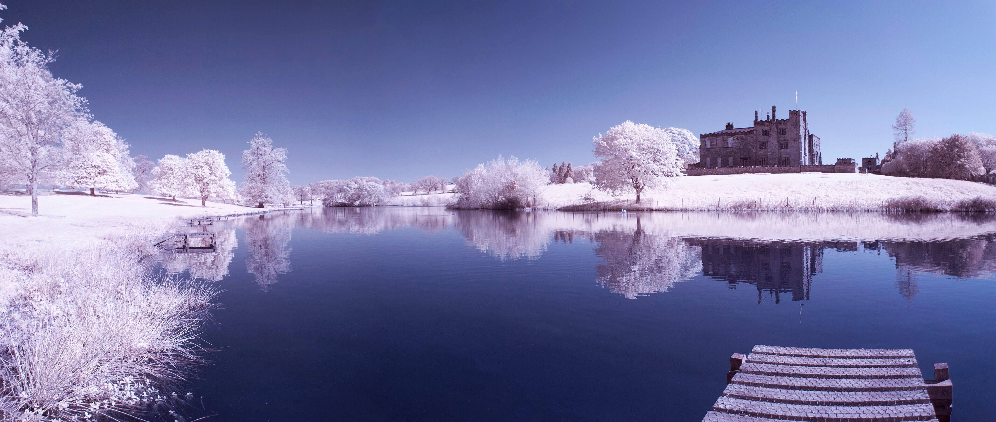 A castle by a calm lake with snow-covered trees and a wooden dock.