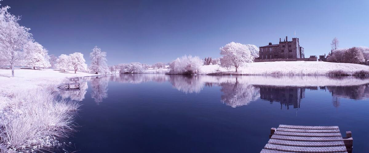 A castle by a calm lake with snow-covered trees and a wooden dock.