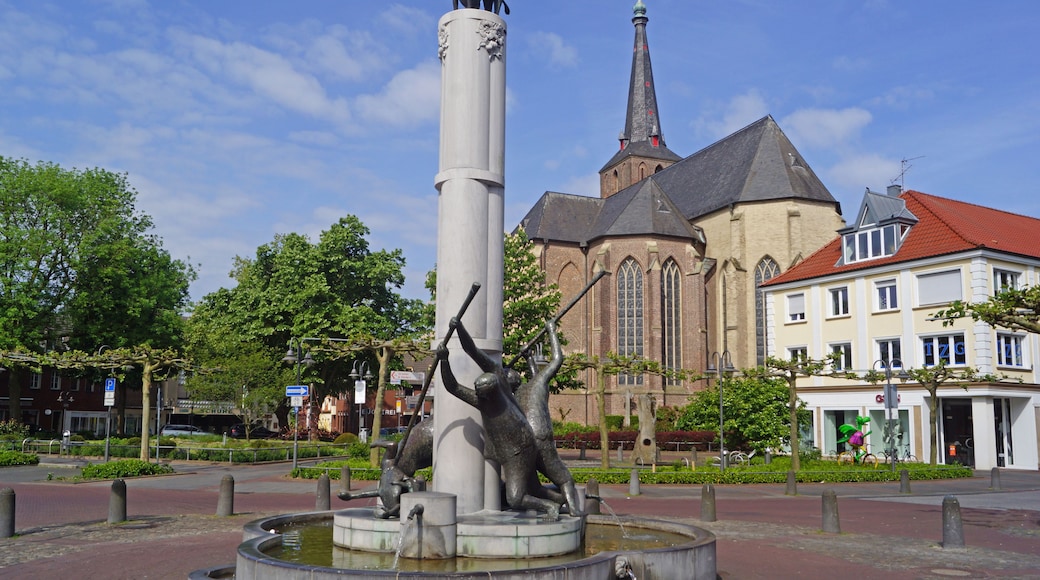 Een standbeeld van een beer op een zuil, een kerk met een torenspits, en een gebouw met een rood dak.