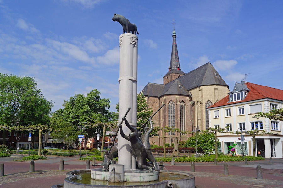 Une statue d’un ours sur une colonne, une église avec une flèche et un bâtiment avec un toit rouge.