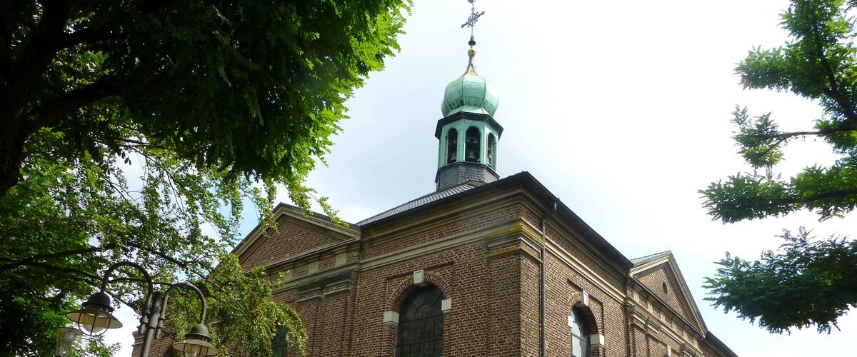 A historic brick church with a green dome and a weather vane.