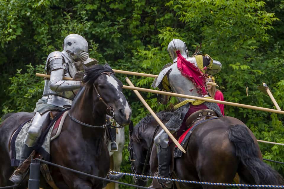 Dos caballeros armados a caballo, uno con armadura plateada y el otro con armadura roja y amarilla, con un bosque de fondo.