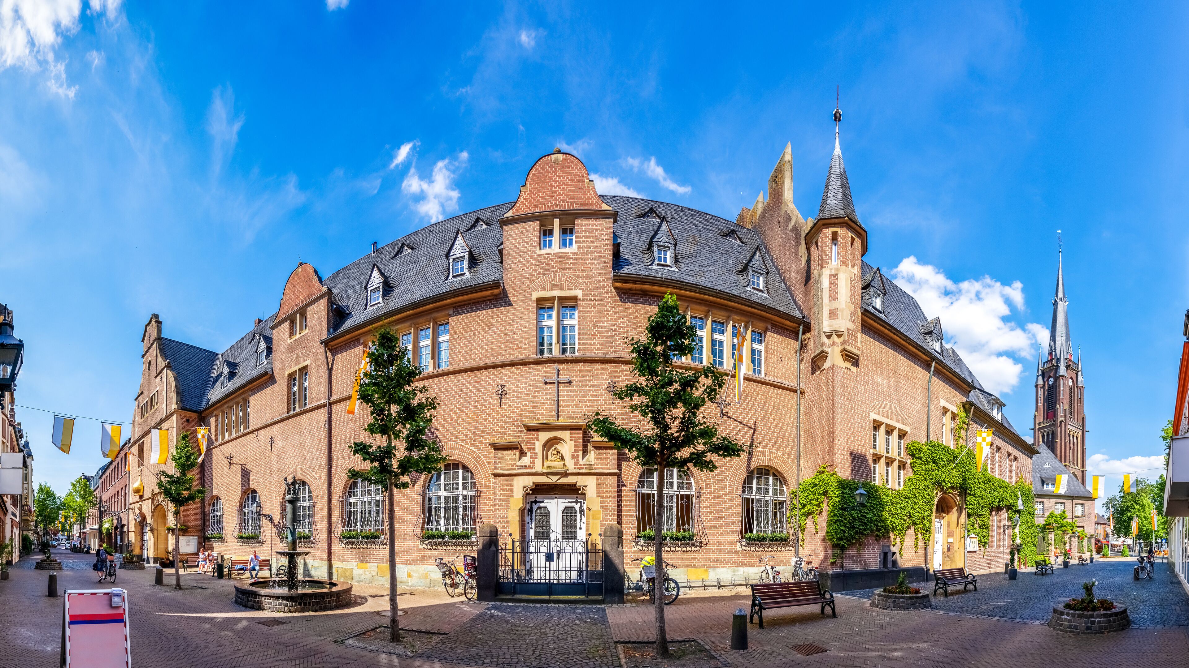 A historic building with a tower, arched windows, and a fountain in a cobblestone square.
