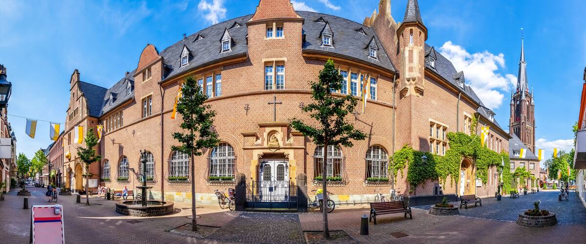 A historic building with a tower, arched windows, and a fountain in a cobblestone square.
