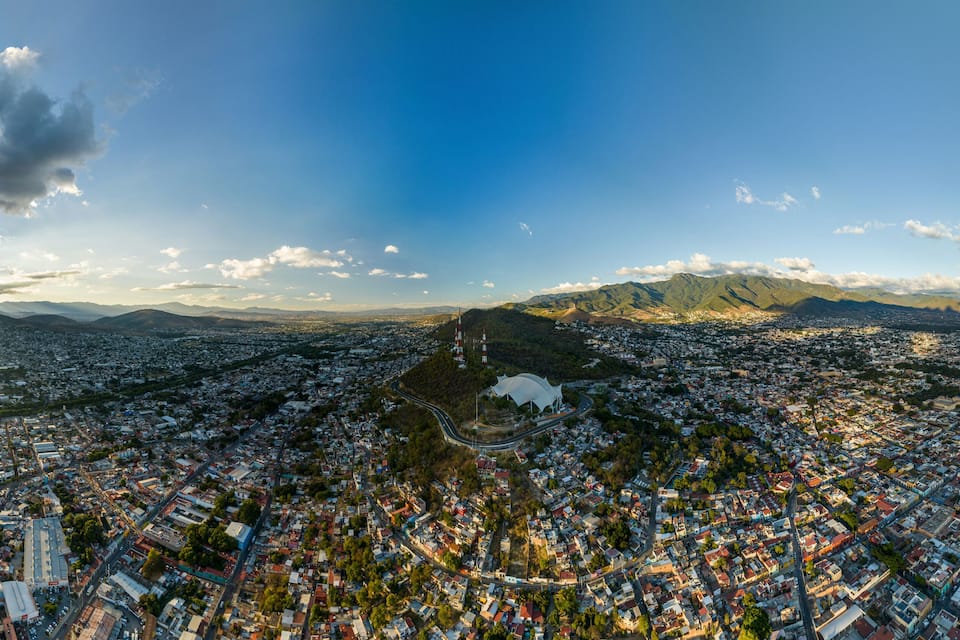 An aerial view of a city with a prominent stadium, dense urban area, and distant mountains under a clear sky.