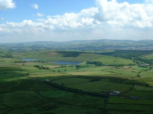 A green valley with fields, a lake, and distant hills.