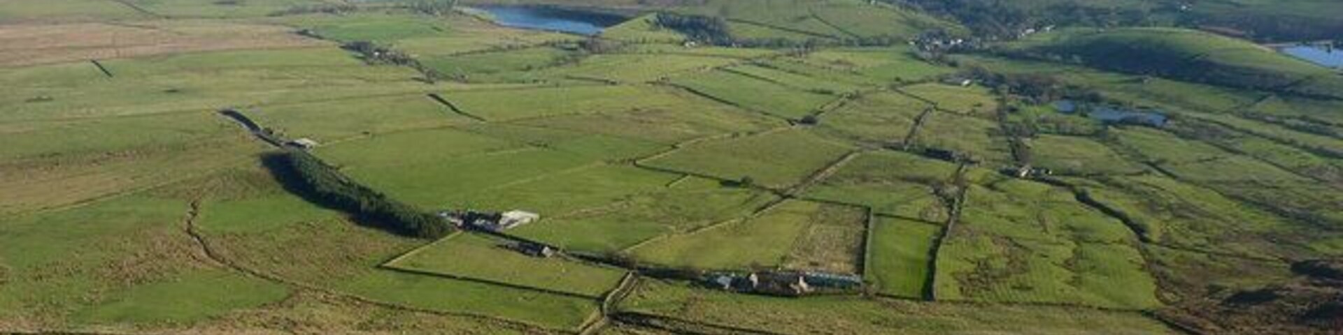 Paisaje rural con campos, una masa de agua pequeña y edificaciones dispersas.