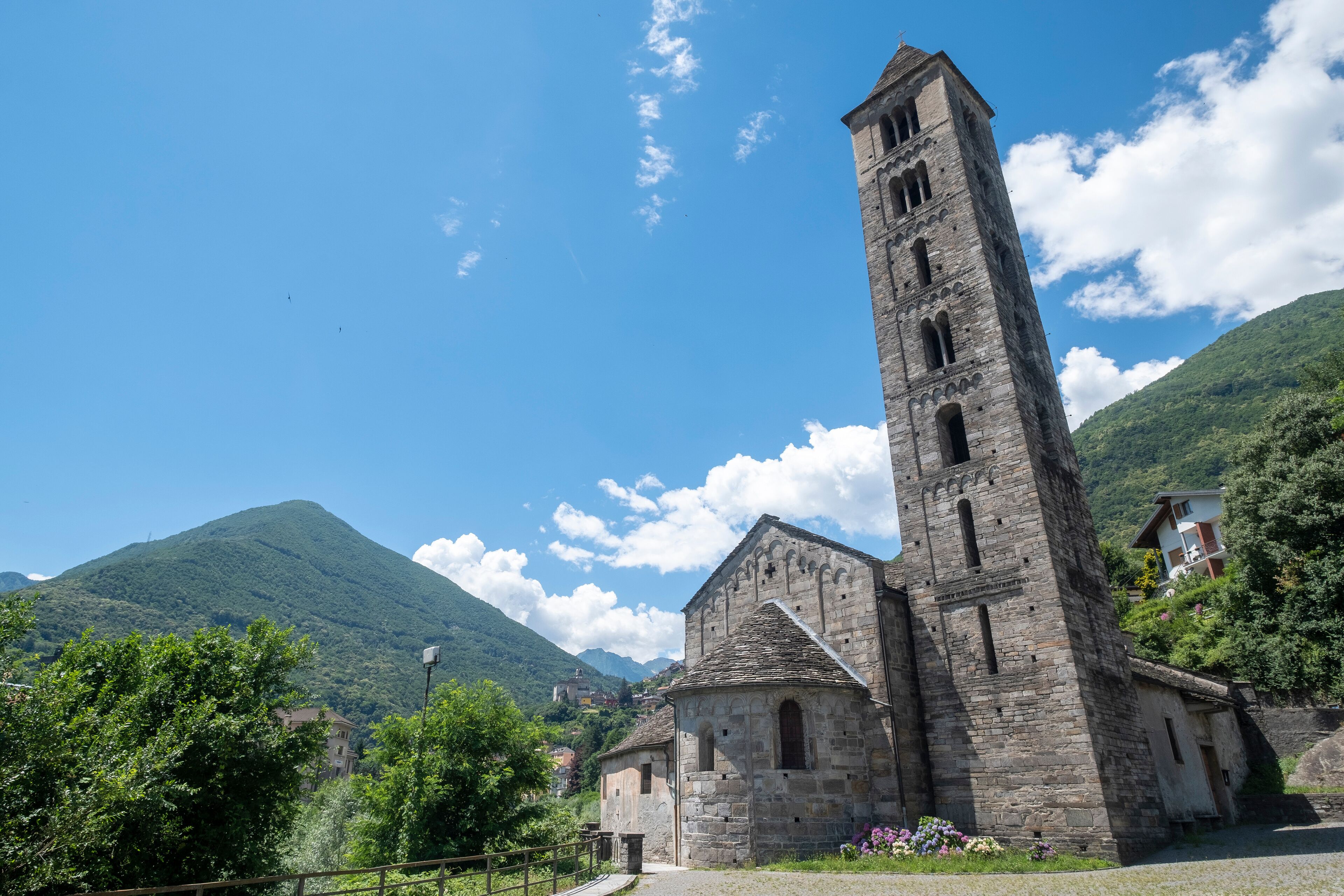 A stone church with a tall bell tower, surrounded by lush green hills and a clear blue sky.