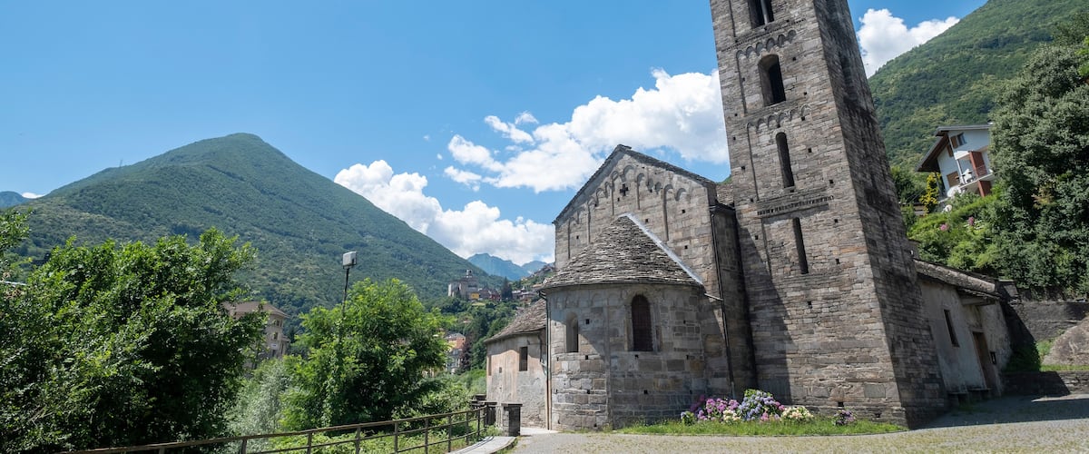 A stone church with a tall bell tower, surrounded by lush green hills and a clear blue sky.