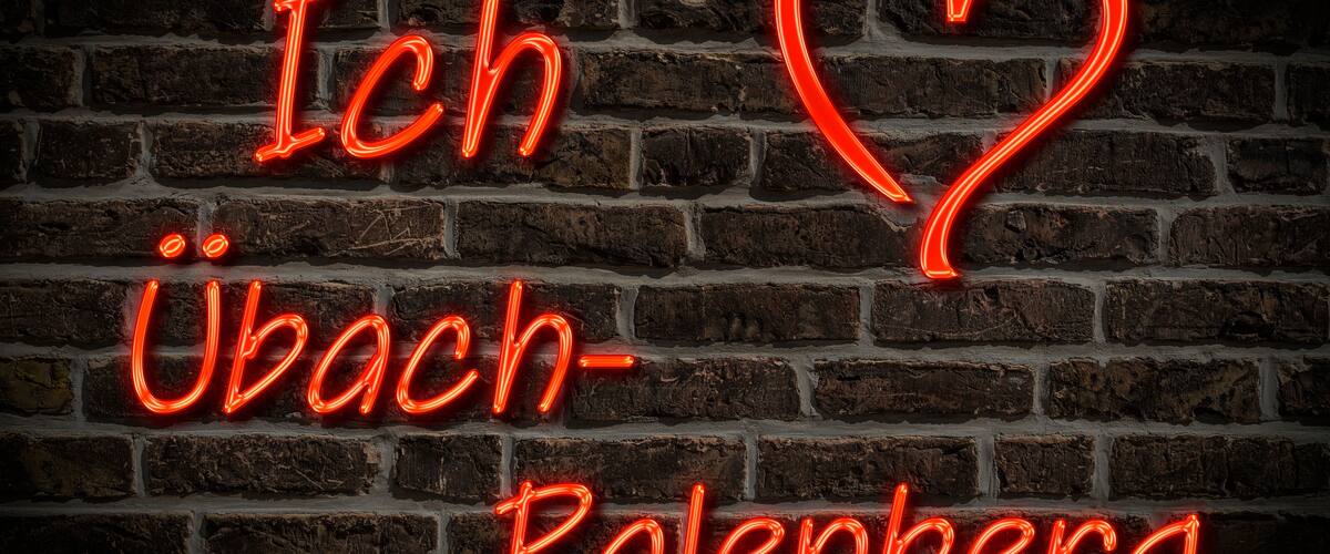 A neon sign spelling "Ich Ubach-Palenberg" on a brick wall.