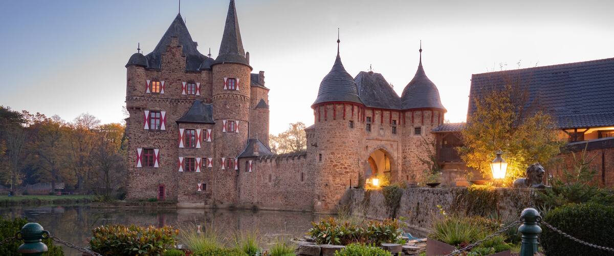 A historic castle with multiple towers, a moat, and a well-maintained garden.