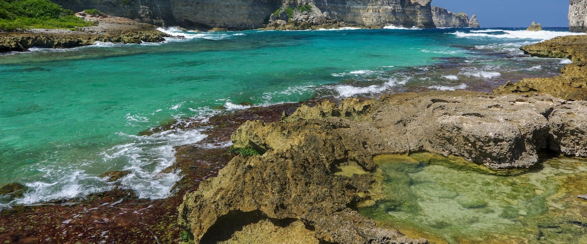 A coastal landscape with clear turquoise waters, rocky shores, and steep cliffs.