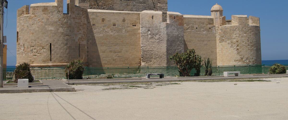 A historic stone fortress with multiple towers and a dome, overlooking a coastal area.