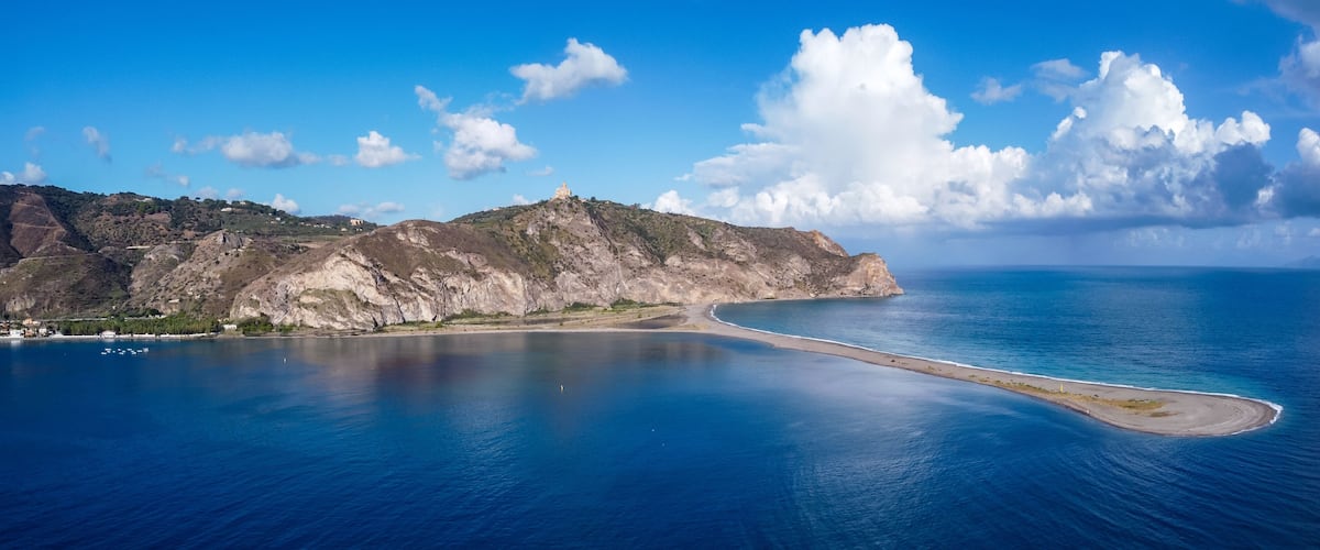 Aerial drone view of Laghetti di Marinello, natural reserve in Sicily, Italy. Sand strip with crystal clear turquoise lagoons, lush Mediterranean vegetation, below a cliff and Tindari Sanctuary.