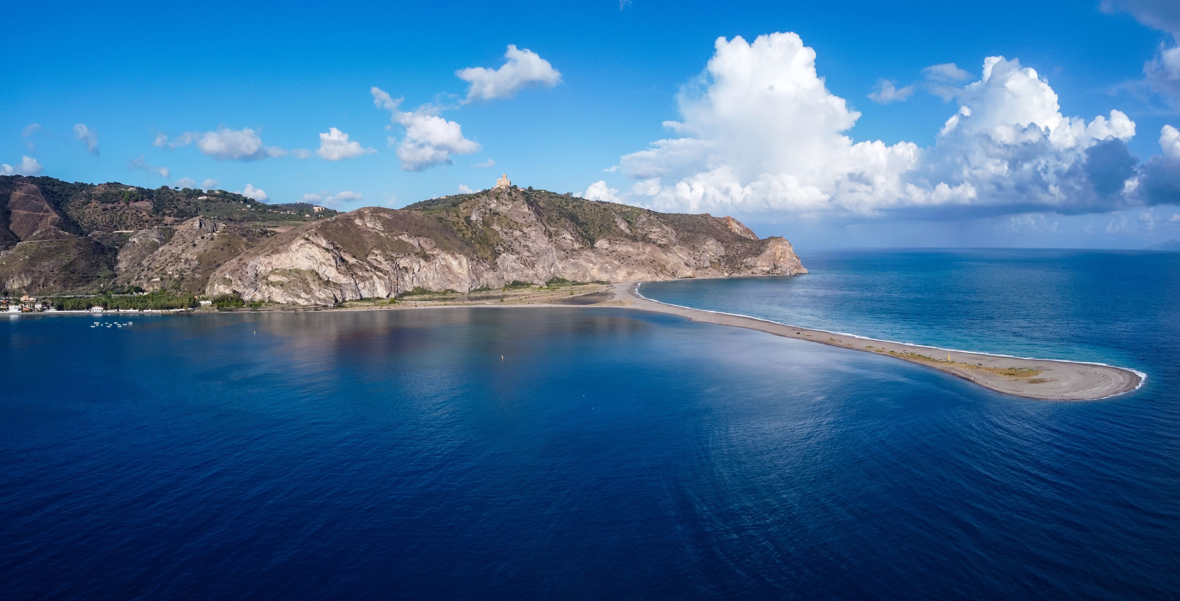 A coastal landscape with a prominent hill, a small island, and a clear blue sea.
