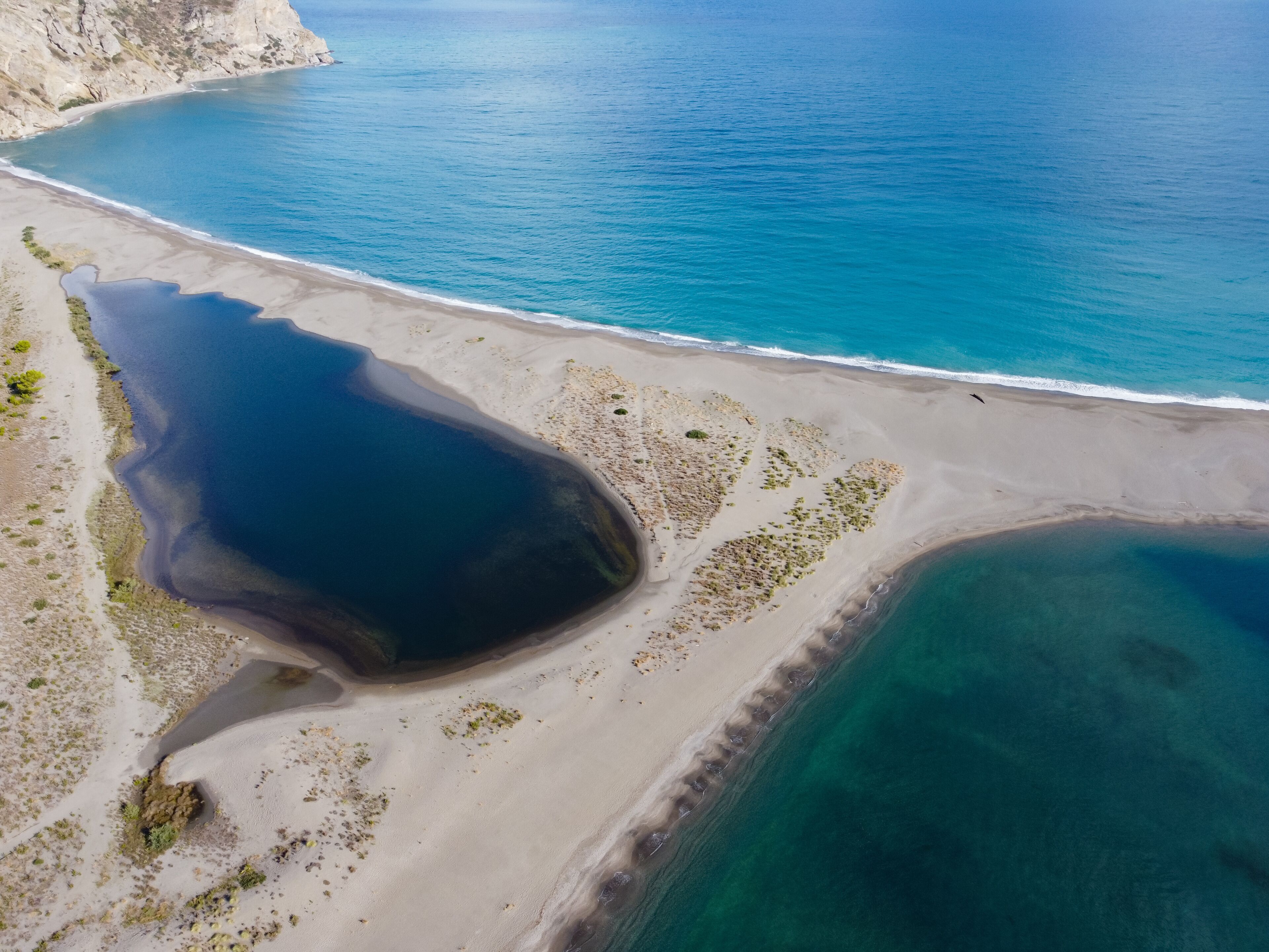 Vista aérea de una zona costera con una gran masa de agua oscura, playa de arena y acantilados rocosos.