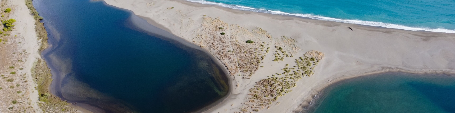 Vista aérea de una zona costera con una gran masa de agua oscura, playa de arena y acantilados rocosos.