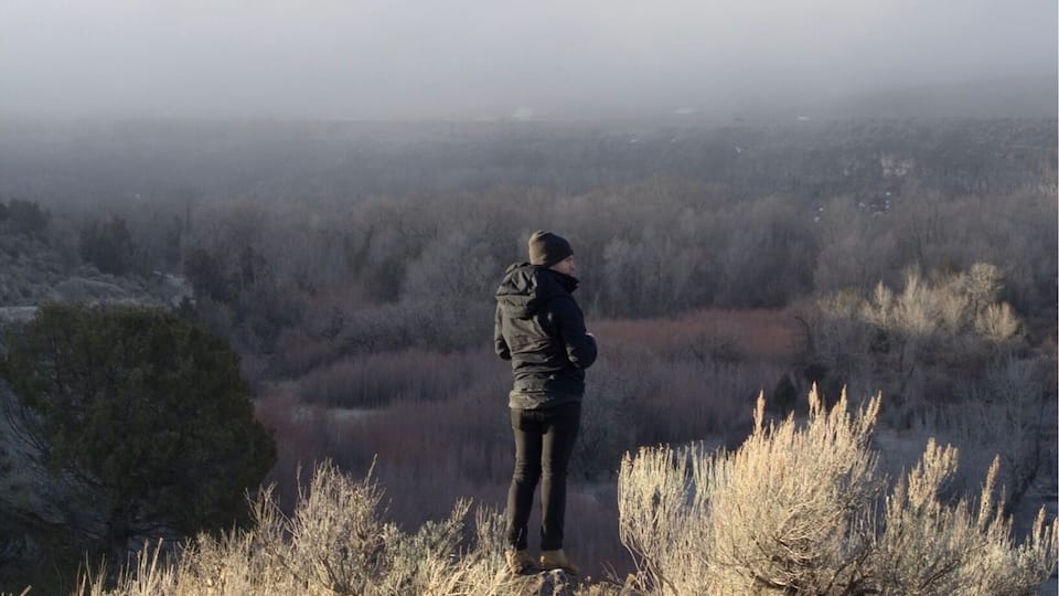 A person standing on a hill overlooking a valley with sparse vegetation and a hazy horizon.
