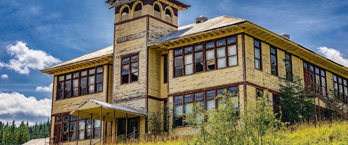 An old, weathered building with a tower labeled "PUBLIC SCHOOL" and a large, open front porch.