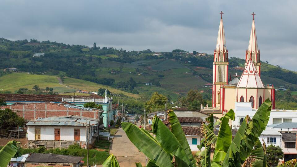 A church with two tall spires, surrounded by lush green hills and banana plants.