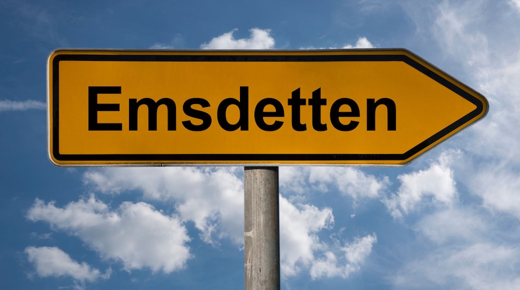 Ein Wegweiser mit dem Schriftzug 'Emsdetten', der nach rechts zeigt, vor blauem Himmel mit vereinzelten Wolken.