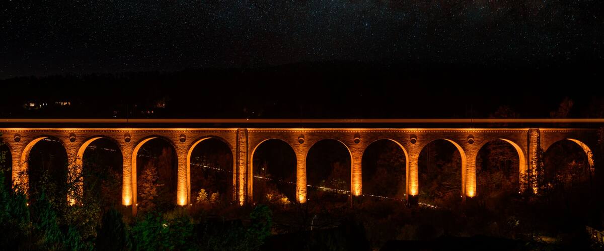 A stone bridge with multiple arches illuminated at night.