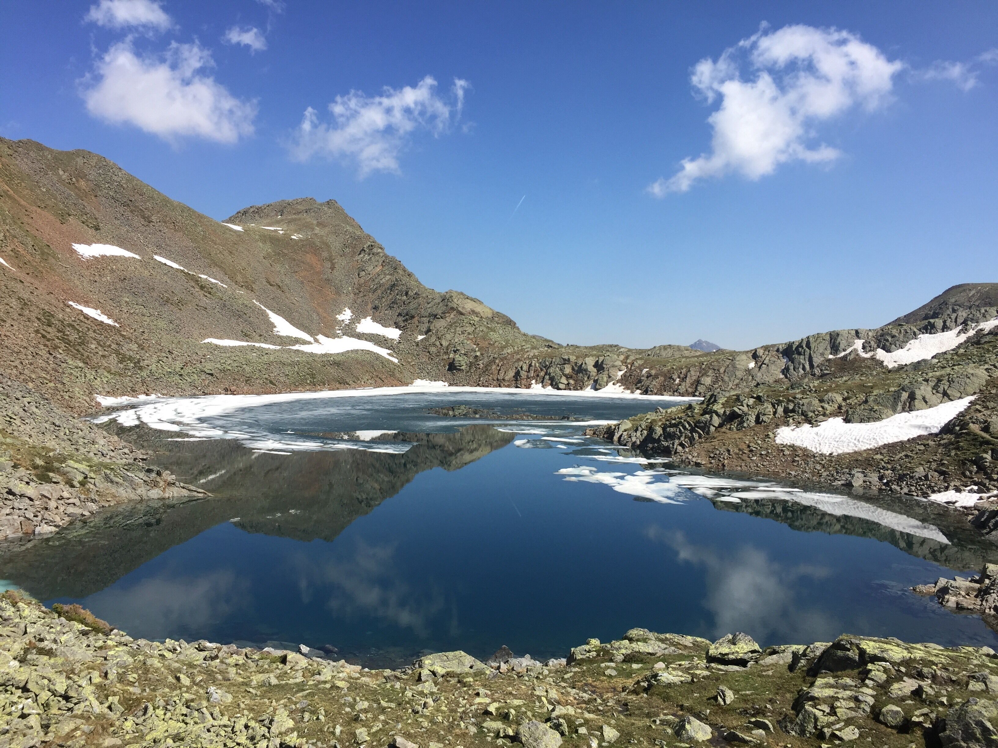 Ein klarer Bergsee, umgeben von felsigem Gelände und Schneeflecken.