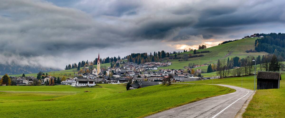A village nestled in a valley with a church, surrounded by green fields and mountains.