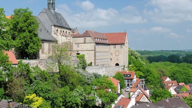 A historic castle with a tall spire, surrounded by lush greenery and traditional houses.