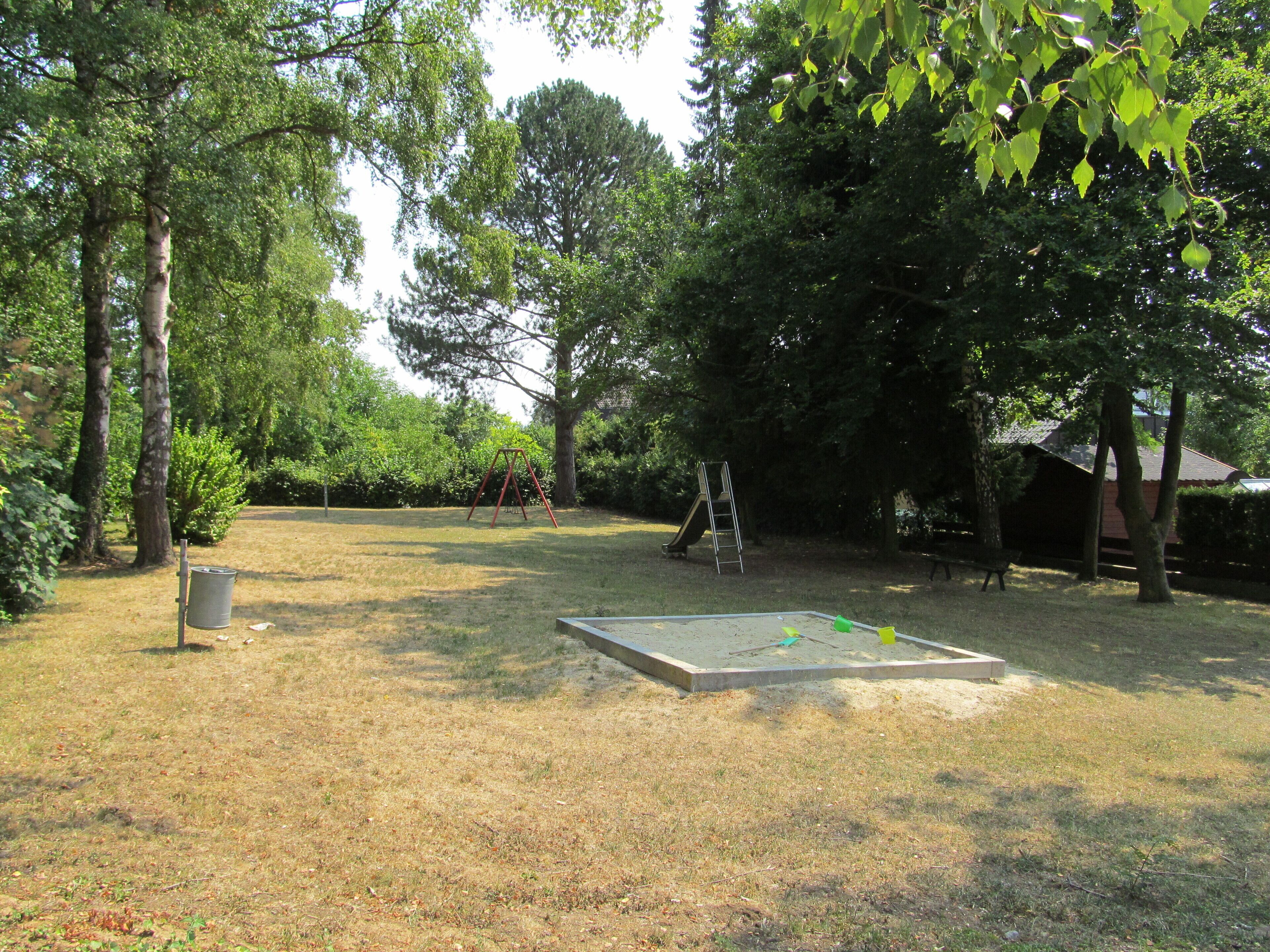 Un parque con un columpio, un tobogán y un arenero.