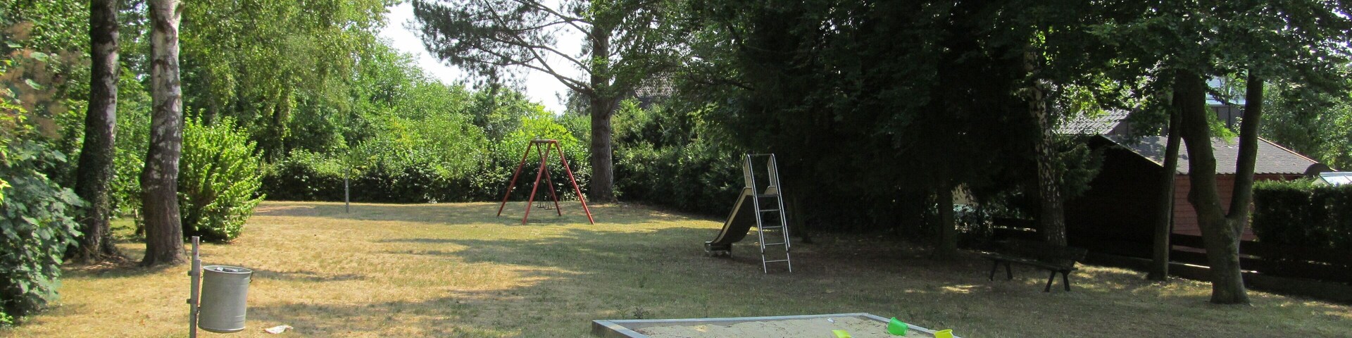 Un parque con un columpio, un tobogán y un arenero.