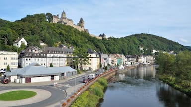 A river with a castle on a hill, a town with colorful buildings, and a roundabout with cars.