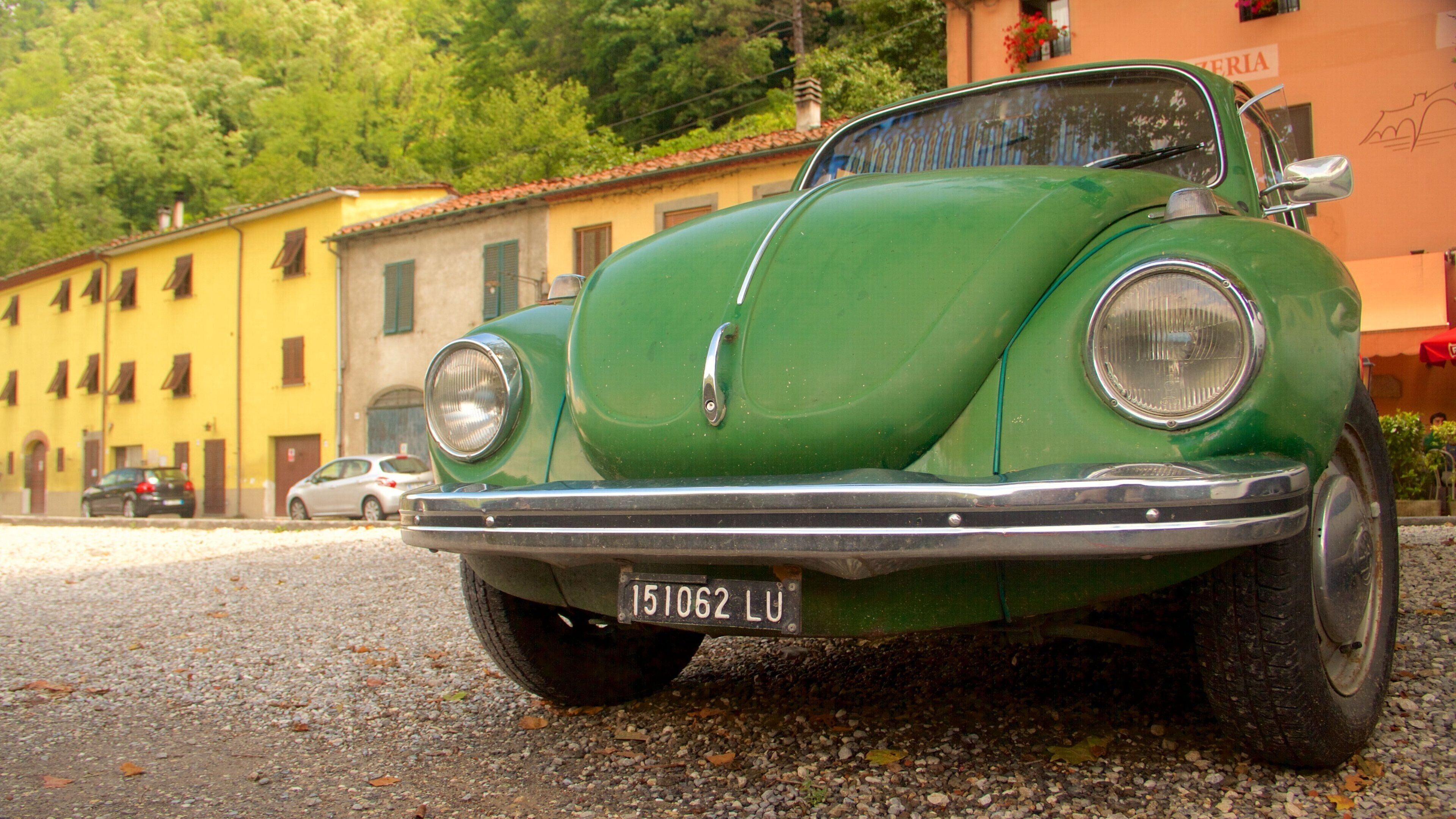 A vintage green car parked on a gravel road with buildings in the background.