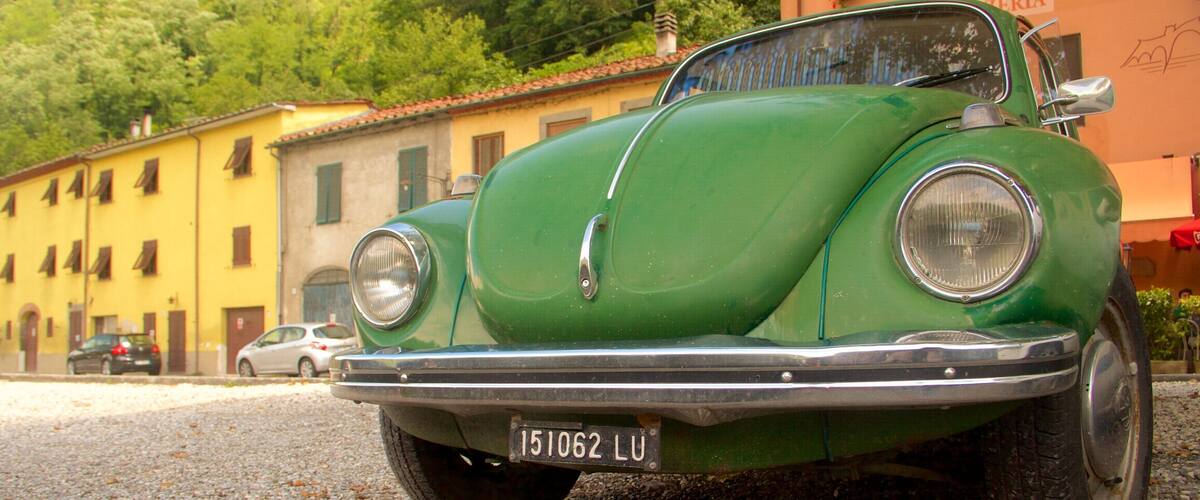 A vintage green car parked on a gravel road with buildings in the background.