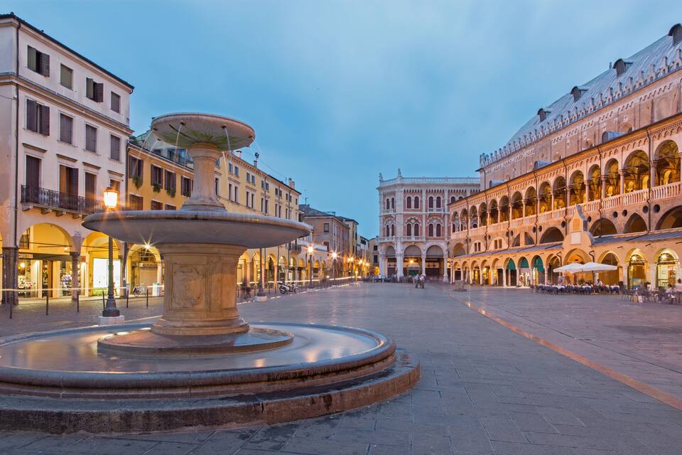 A historic square with a central fountain, ornate buildings, and a clear sky.