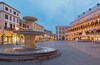 Una plaza histórica con una fuente central, edificios ornamentados y cielo despejado.