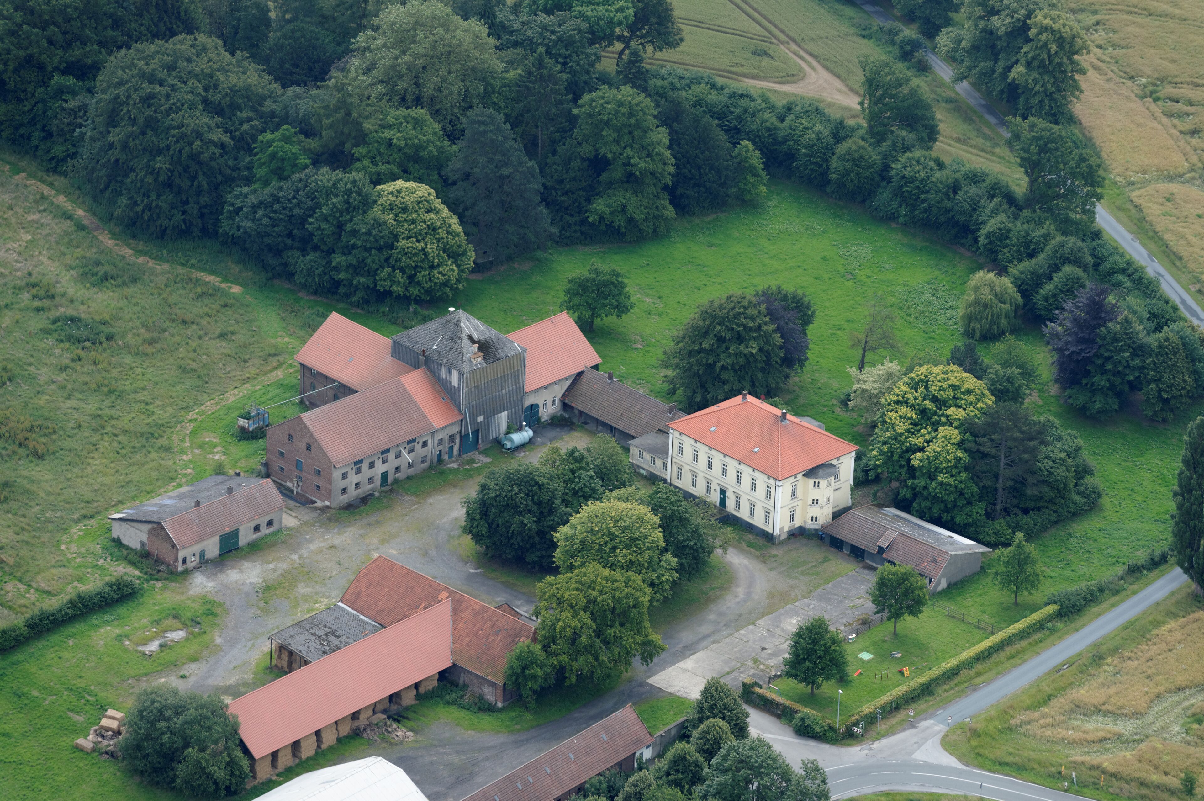 An aerial view of a rural estate with multiple buildings, green fields, and a winding road.