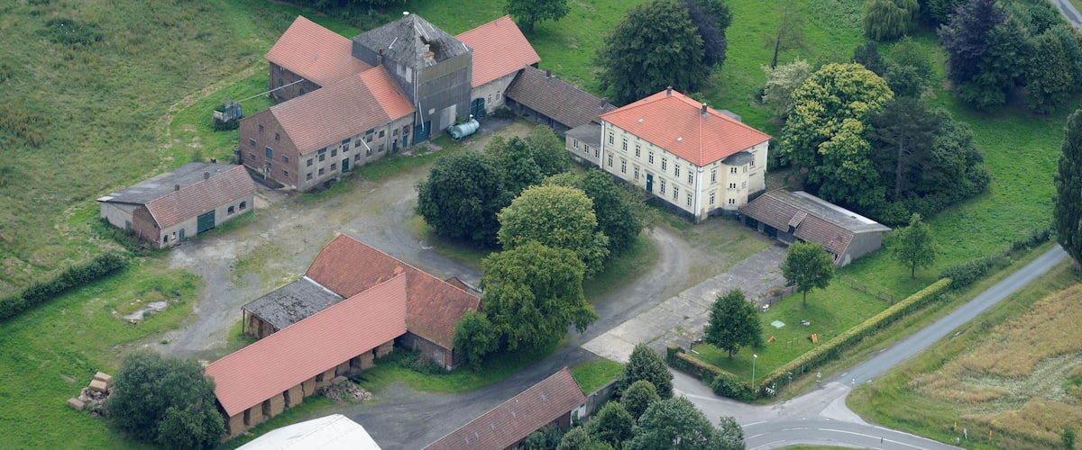 An aerial view of a rural estate with multiple buildings, green fields, and a winding road.