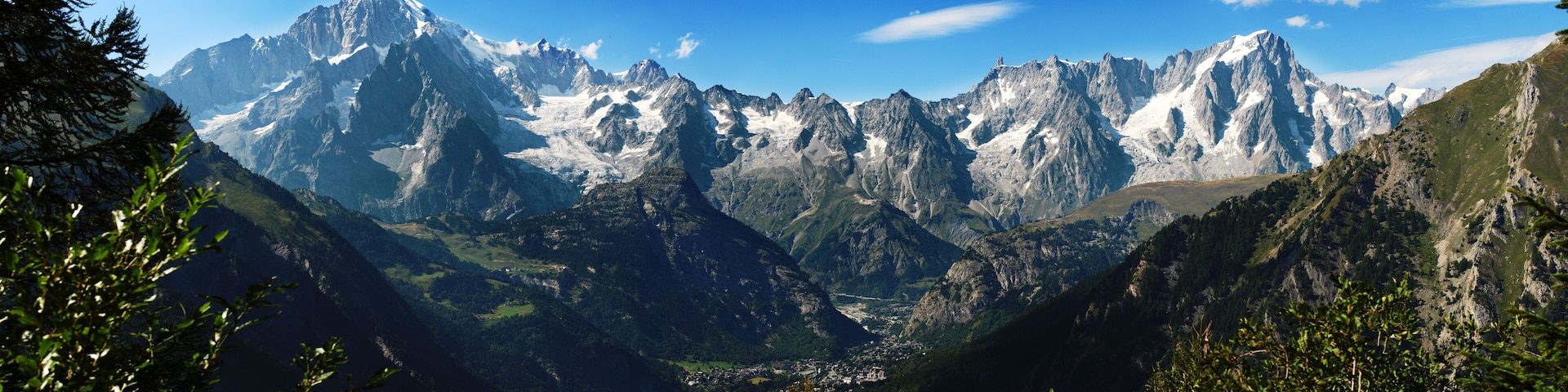 A mountainous landscape with snow-capped peaks, dense forests, and a valley with a small settlement.