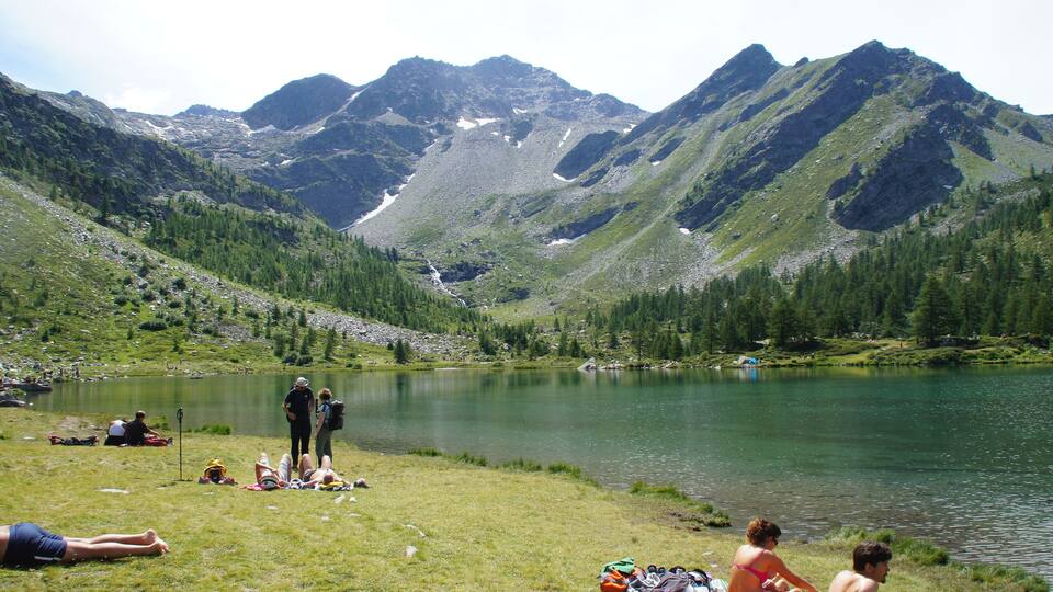A lake surrounded by mountains with people relaxing on the grass.