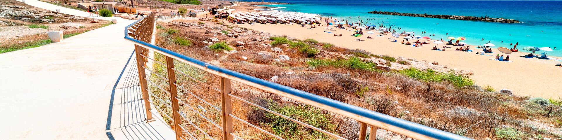 View from Paphos seaside promenade on Turquoise waters Mediterranean Sea, Venus Beach with relaxing tourists. The most beautiful beaches on holiday island Cyprus, Paphos.