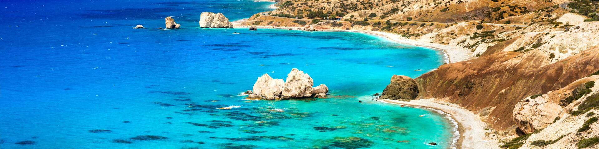 A coastal landscape with clear turquoise waters, rocky outcrops, and a winding road along the hillside.