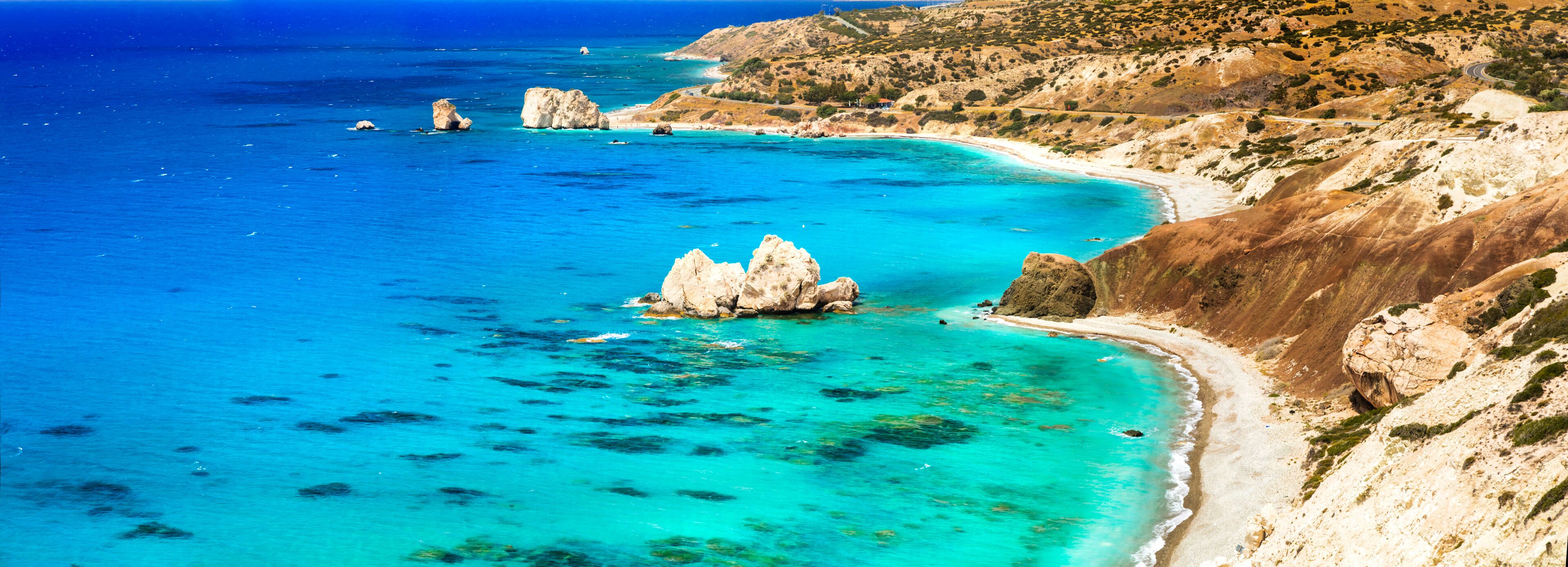 A coastal landscape with clear turquoise waters, rocky outcrops, and a winding road along the hillside.