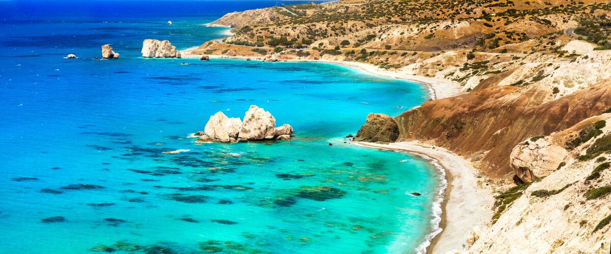 A coastal landscape with clear turquoise waters, rocky outcrops, and a winding road along the hillside.