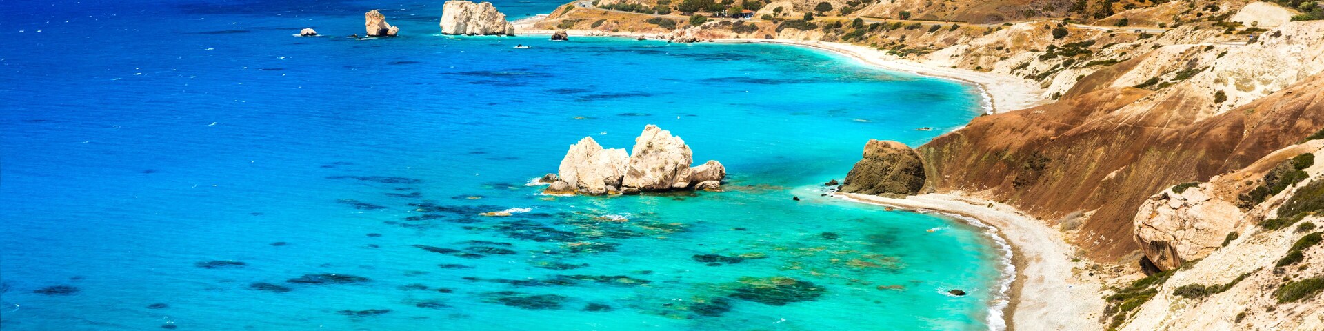 A coastal landscape with clear turquoise waters, rocky outcrops, and a winding road along the hillside.