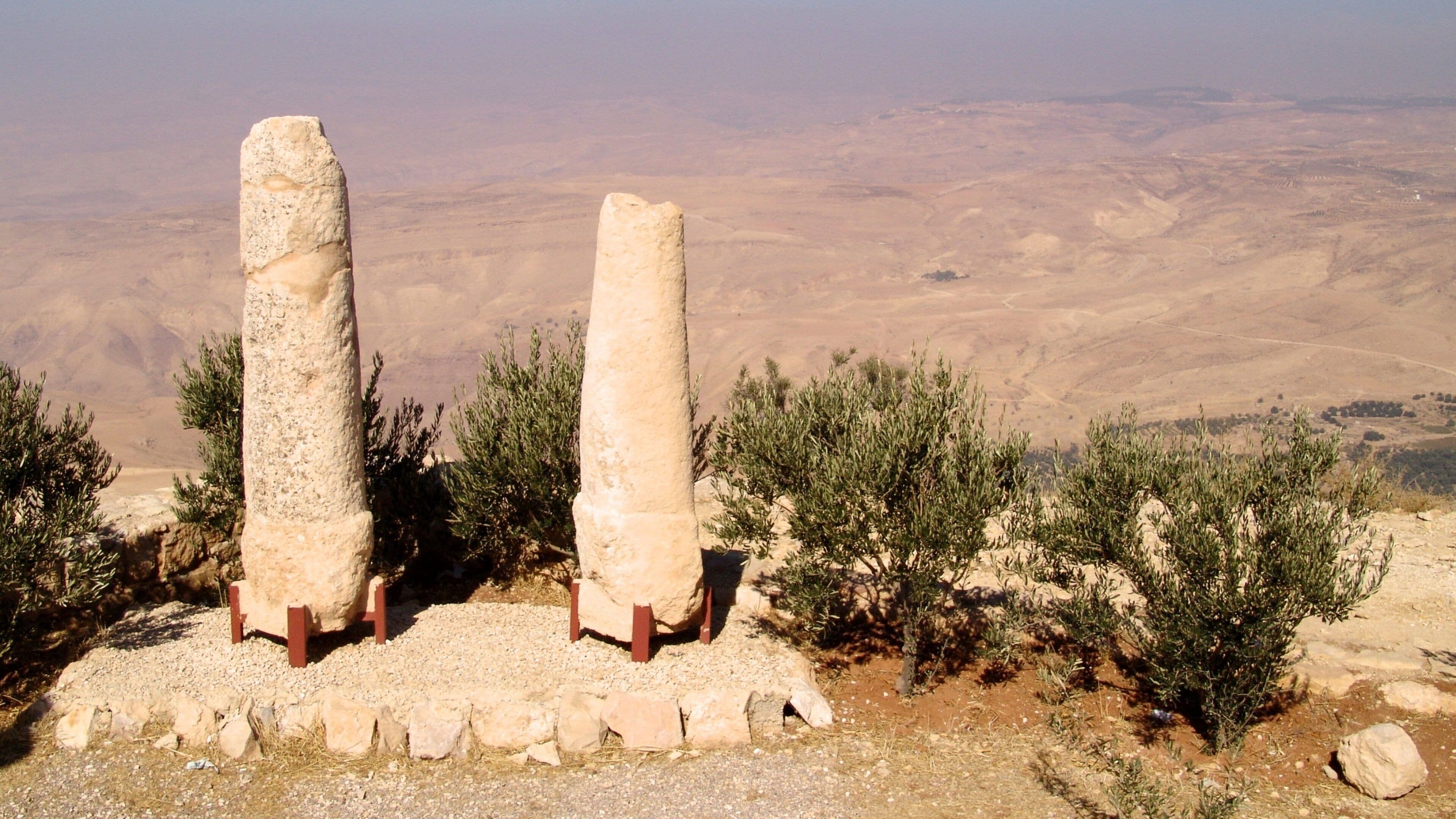 Two tall stone pillars in a desert landscape with sparse vegetation.